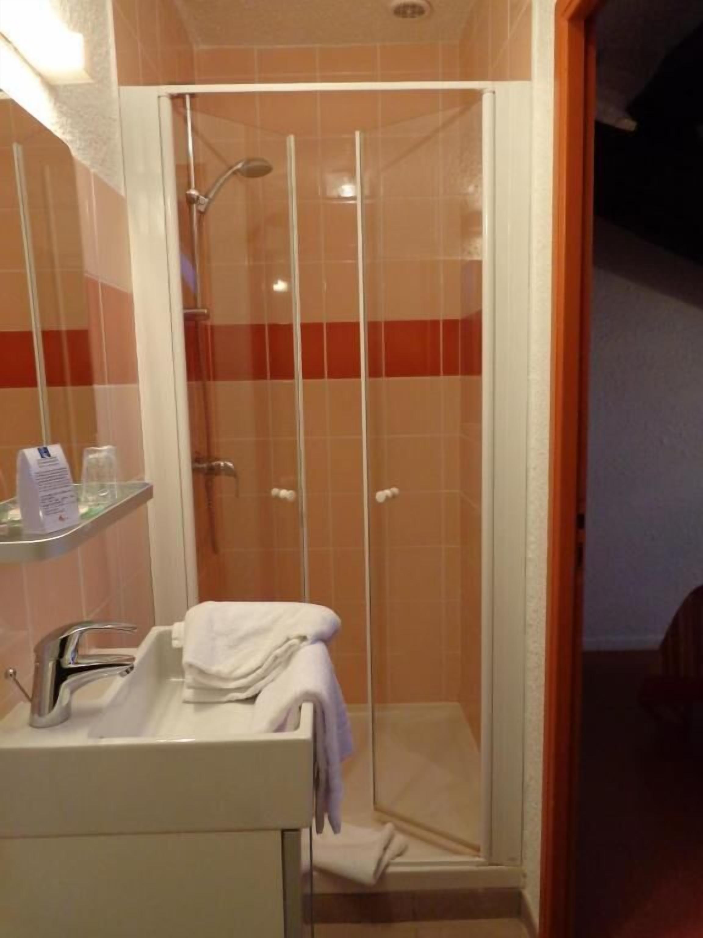 A shower enclosure with a glass door, a sink with a towel, and a shelf with toiletries.