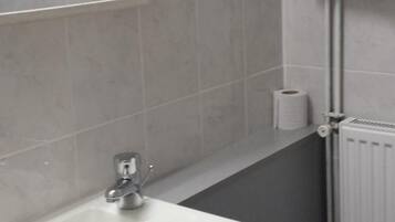 A bathroom with a white sink, a mirror, a towel, a toilet paper roll, and a radiator.