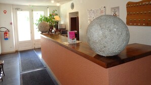 A reception area with a stone sculpture, a fire extinguisher, a clock, and a bulletin board. - Citotel Du Tigre (Verdun)