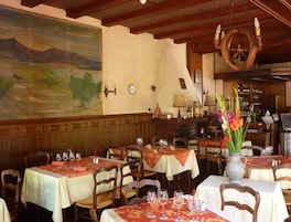 Interior de restaurante con paneles de madera, mesas dispuestas con copas de vino y un cuadro de paisaje de gran tamaño en la pared.