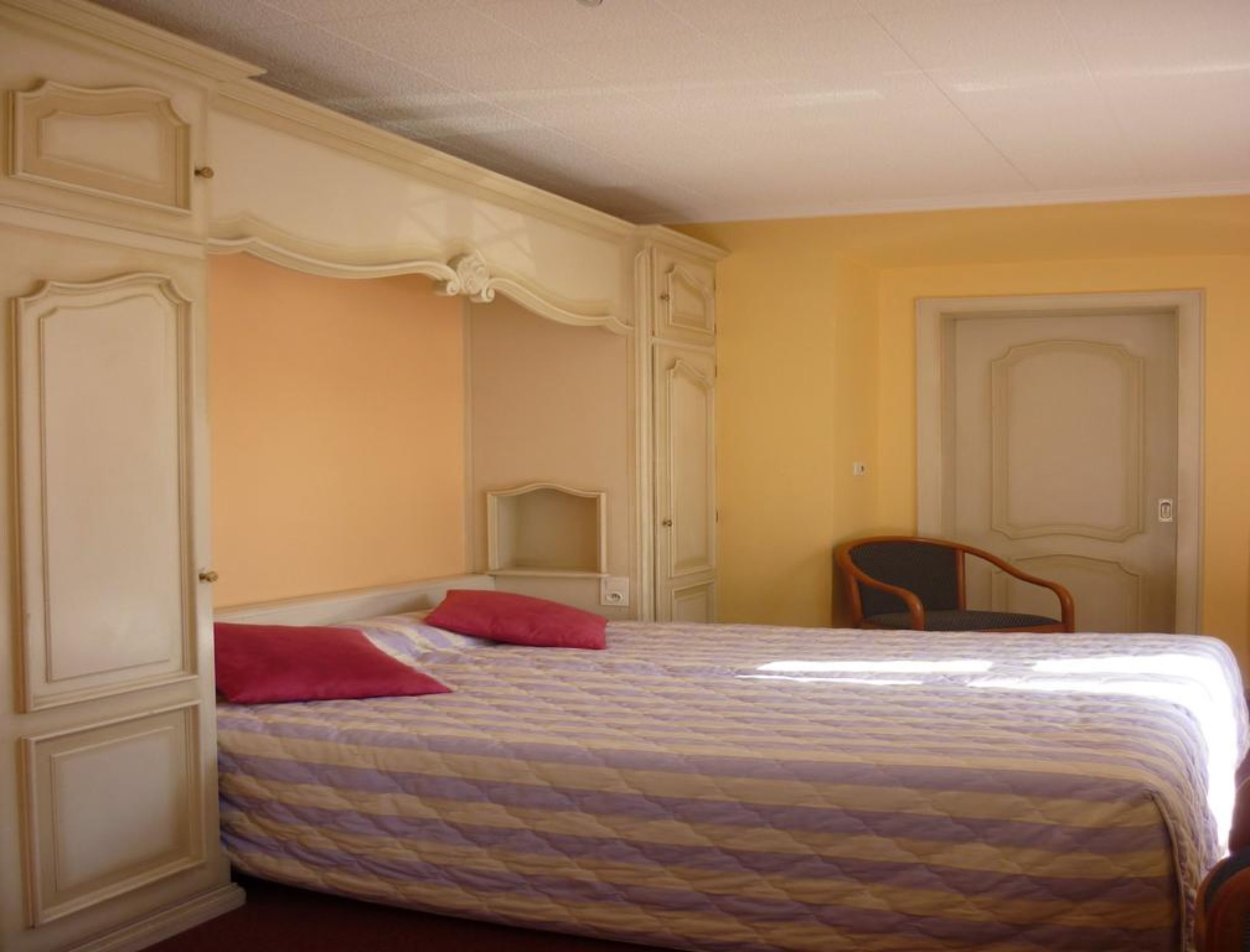 A bedroom with a bed, two chairs, and a wardrobe.
