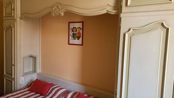 Un dormitorio con una cama, dos almohadas rojas, un cuadro enmarcado en la pared y una puerta blanca.