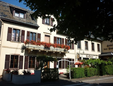 A hotel with a balcony adorned with red flowers, a sign for a restaurant, and a well-maintained garden area.