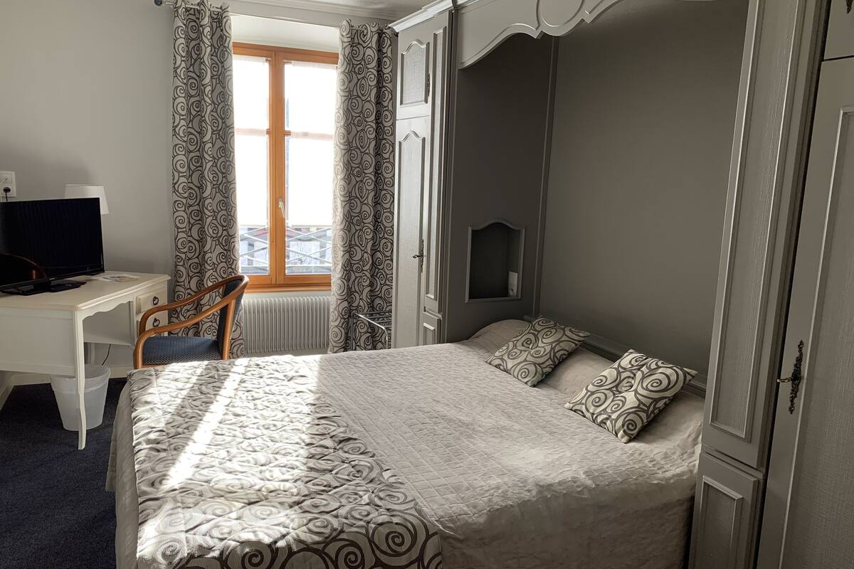 Habitación de hotel con cama, escritorio, computadora, silla y ventana con cortinas.