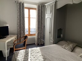 Una habitación de hotel con cama, escritorio con televisor, una silla y cortinas.