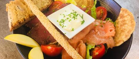 A plate with various food items including bread, salmon, tomatoes, and a small bowl of sauce.