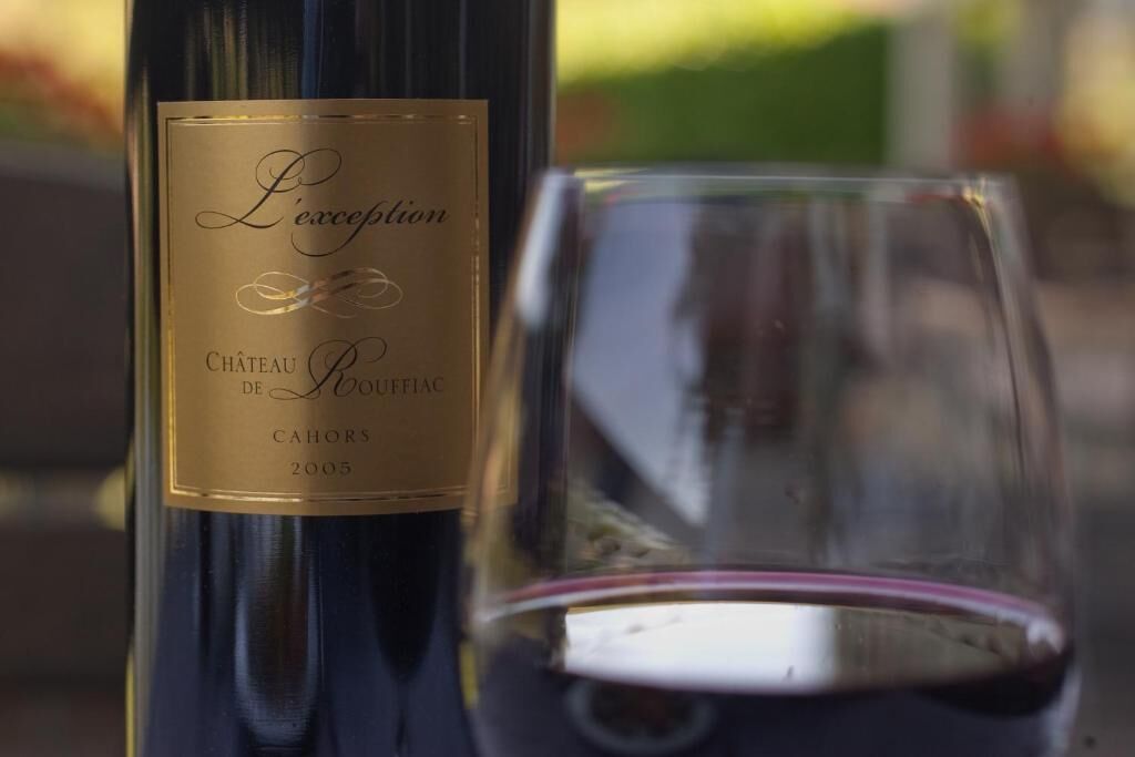En flaske L'Excellence vin med etiket og et glas fyldt med rødvin.