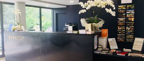A reception desk with a dark counter, a nameplate, a printer, and a bulletin board with photos and papers.