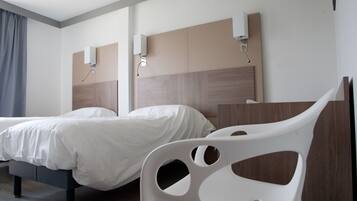 A hotel room with two beds, a white chair, and a wooden headboard.