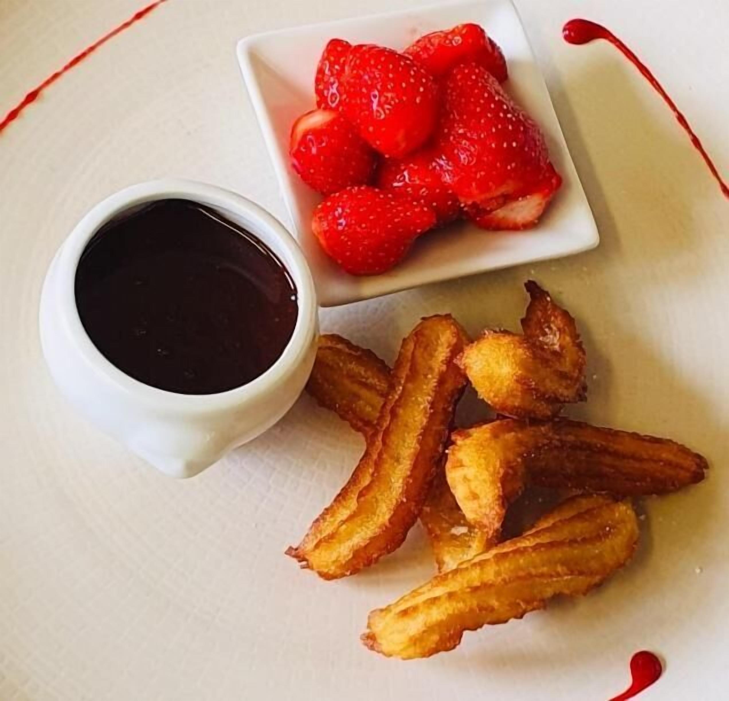 Un plato con papas fritas, un tazón pequeño de fresas y una taza de salsa.
