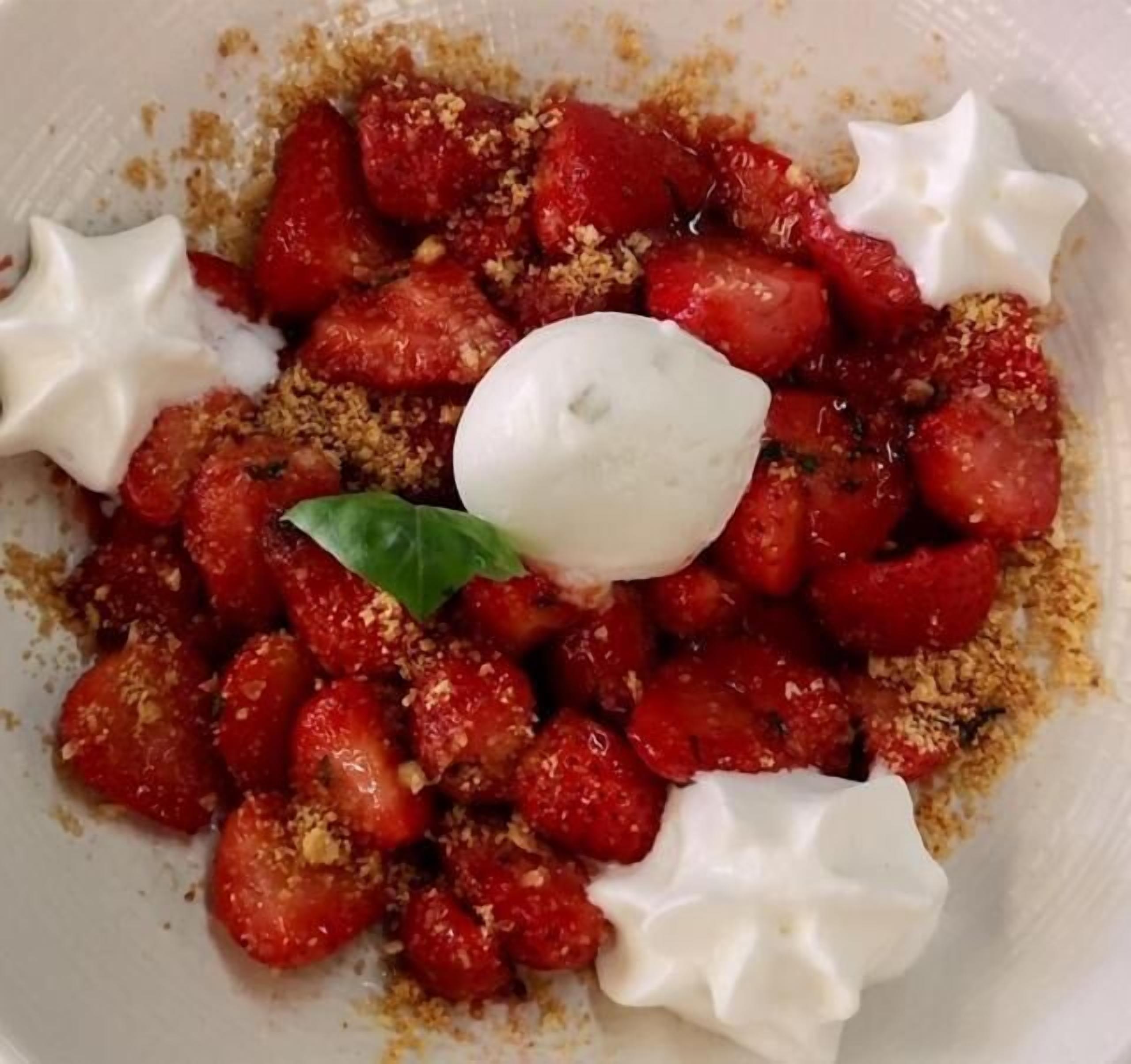 A plate of food with strawberries, crumbled cheese, and a dollop of cream.