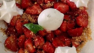 Un plato de comida con fresas, queso desmenuzado y una cucharada de crema.