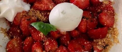 A plate of food with strawberries, crumbled cheese, and a dollop of cream.