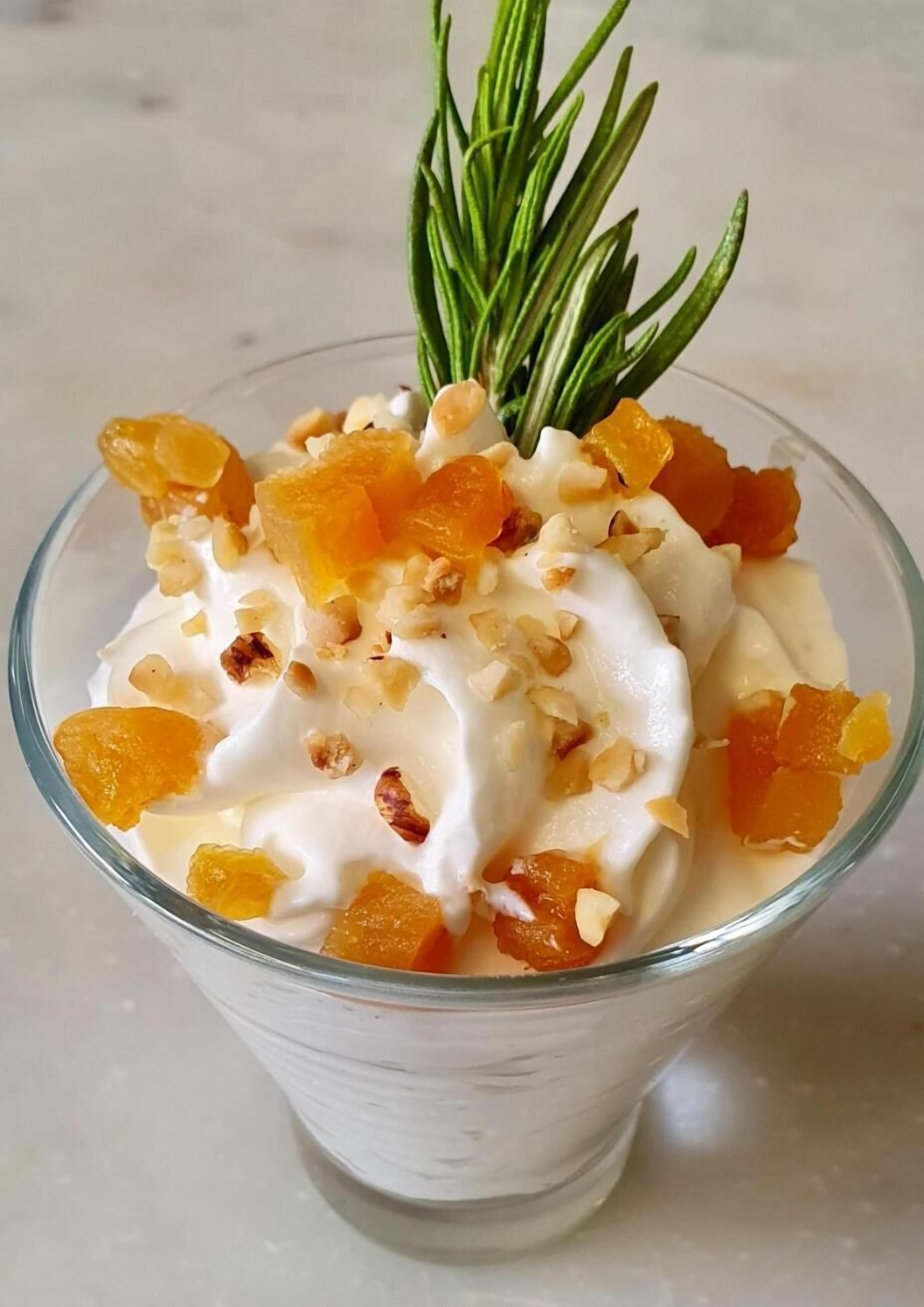 Un dessert servi dans un bol en verre transparent, garni d’une branche de romarin.