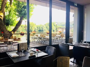 A restaurant with outdoor seating overlooking a lake, featuring a large tree and a view of the water. - La Chartreuse Logis Hotel Restaurant (Cahors)