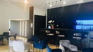 Zona de bar moderna con mostrador negro, sillas azules y grises, y una lámpara colgante.