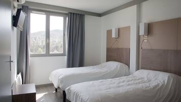 Camera d'albergo con due letti singoli, una TV a muro, una finestra con tende e vista sull'esterno.