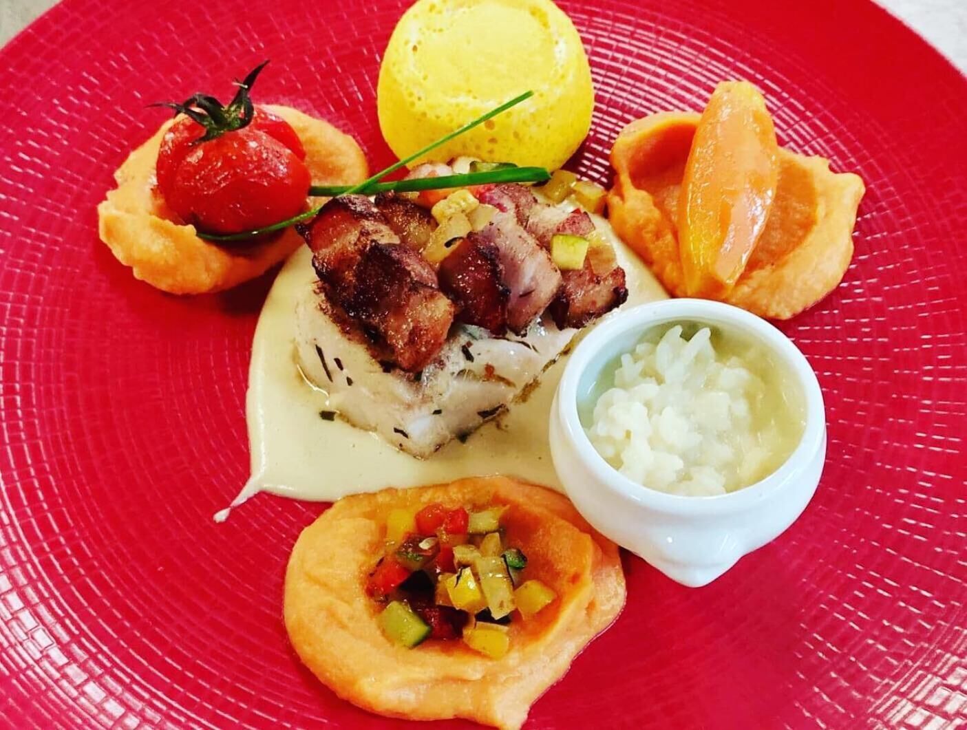 Un plato con varios alimentos, incluyendo un trozo de pescado, un tomate, un limón y un tazón pequeño de arroz.
