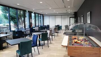 Una cafetería moderna con mesas y sillas, ventanas amplias y una zona de exhibición de alimentos.