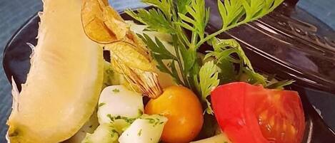 A bowl of food with various vegetables and a leafy herb.