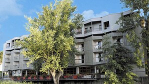 Un edificio moderno de varios pisos con balcones, ubicación junto al río y un restaurante en la planta baja.