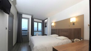 Habitación de hotel con cama, escritorio, silla, televisor y ventana con cortinas.