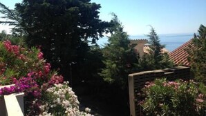 A view of a coastal area with a building with a tiled roof, surrounded by greenery and flowers. - L'Oasi (Dorgali)