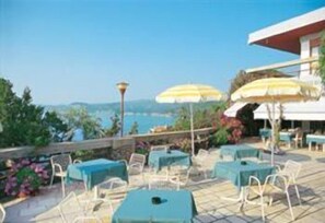 Eine Außenpatio mit Tischen, Stühlen und Sonnenschirmen, mit Blick auf das Meer.