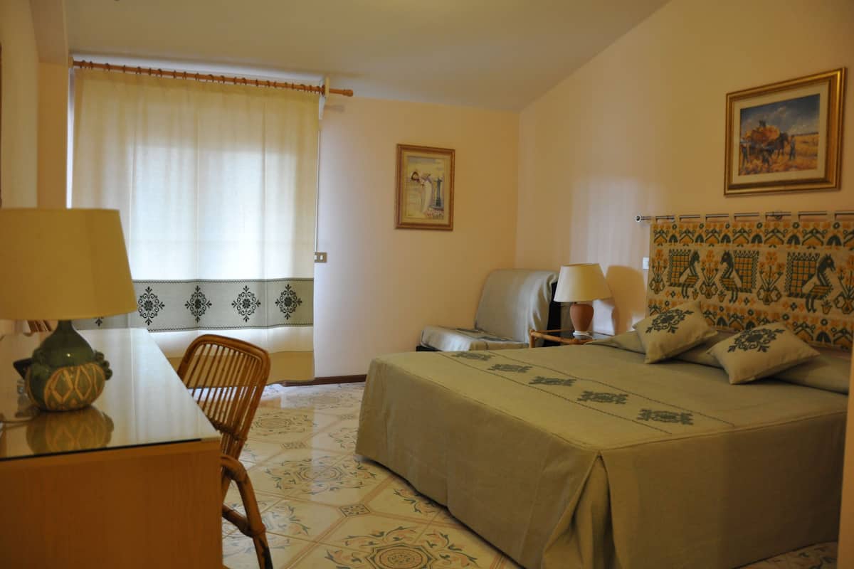 Habitación de hotel con cama, escritorio, silla y ventana con cortinas.