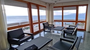A room with a view of the sea, furnished with black chairs and tables, and large windows with curtains. - L'Oasi (Dorgali)