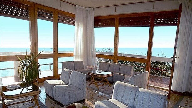 A spacious balcony with a view of the sea, furnished with grey sofas and a glass coffee table. - L'Oasi (Dorgali)