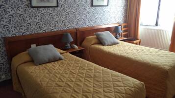 Ein Hotelzimmer mit zwei Betten, jeweils mit gesteppter Bettdecke und Kissen, einem Holz-Kopfteil, Nachttischen mit Lampen und gerahmten Bildern an der Wand.
