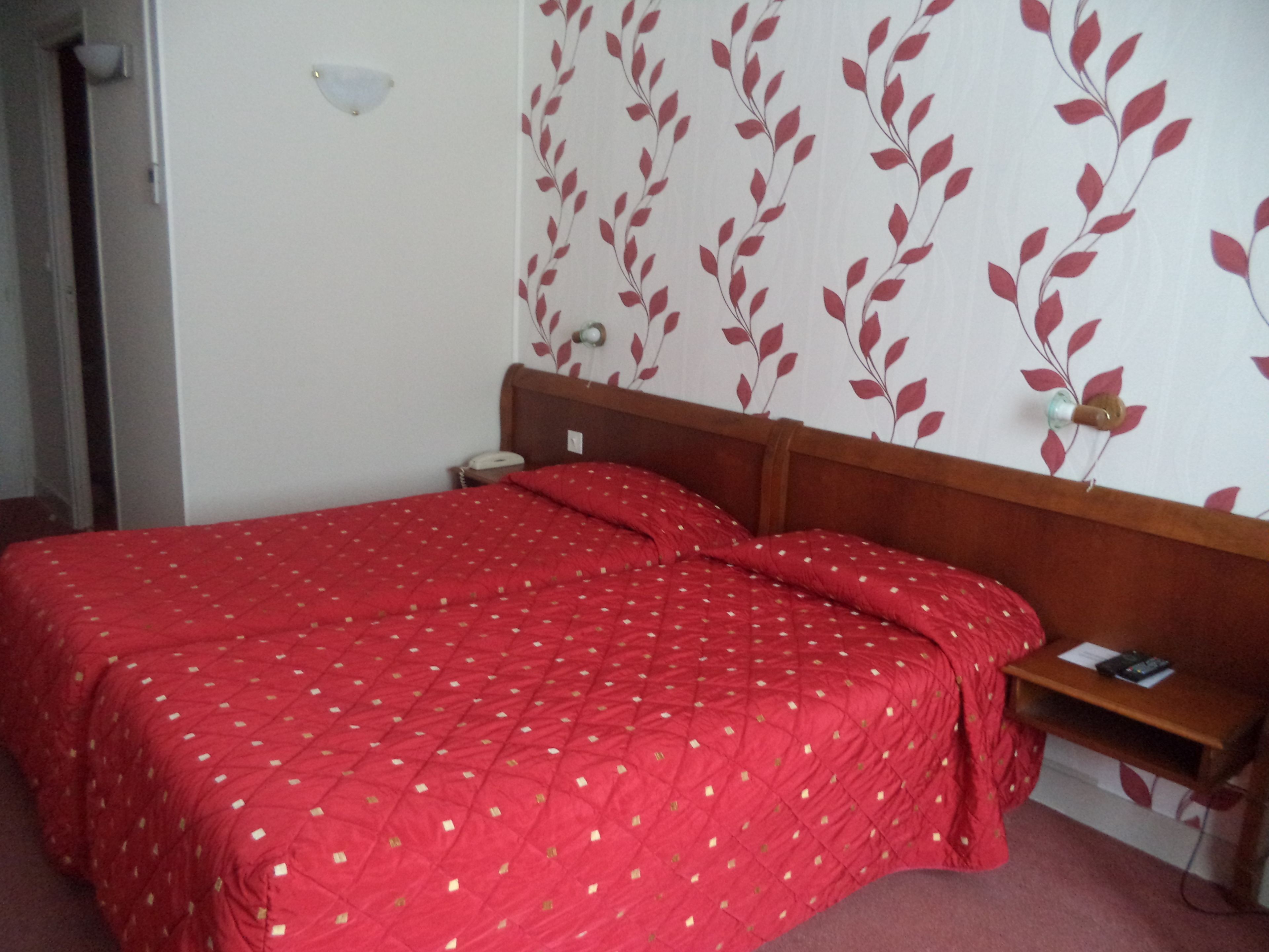 A room with a bed, a nightstand, a wall-mounted lamp, and a wall with a leaf pattern.