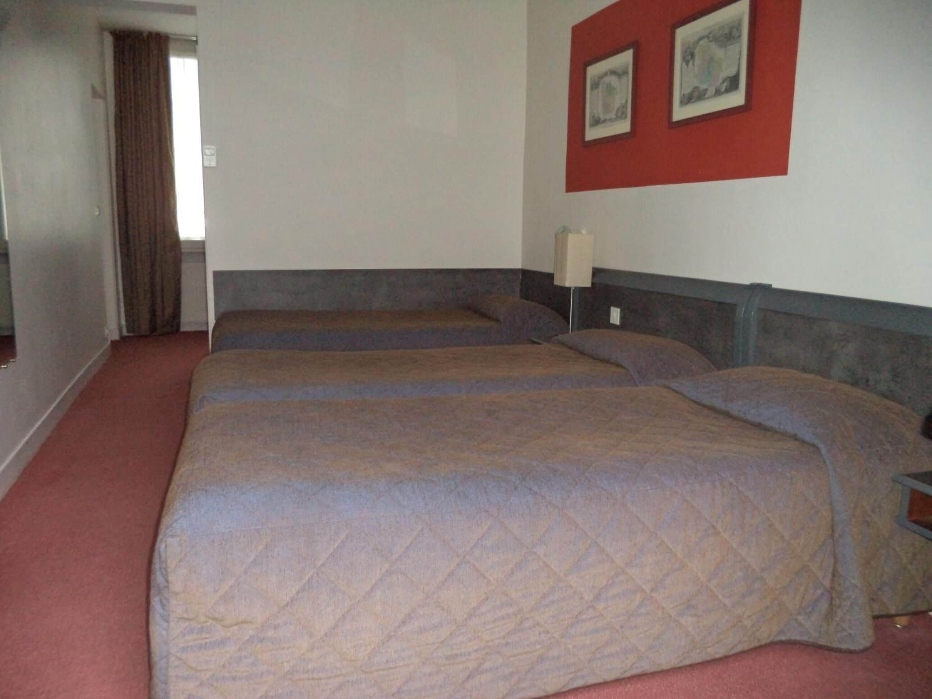 Une chambre d’hôtel avec deux lits, un mur rouge orné de tableaux encadrés et une moquette rouge.