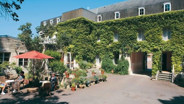 A courtyard with a building covered in ivy, outdoor seating, and potted plants. - Citotel Avallon Vauban (Avallon)
