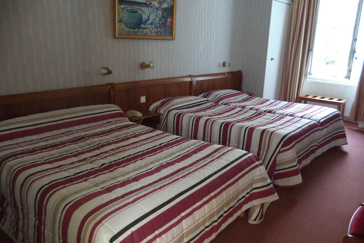 A hotel room with two beds, a wooden headboard, a painting on the wall, and a window with curtains.
