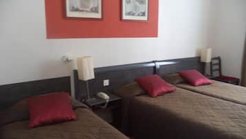 Une chambre d’hôtel avec deux lits, chacun agrémenté d’un oreiller rouge, une table de chevet avec une lampe et deux tableaux encadrés au mur.