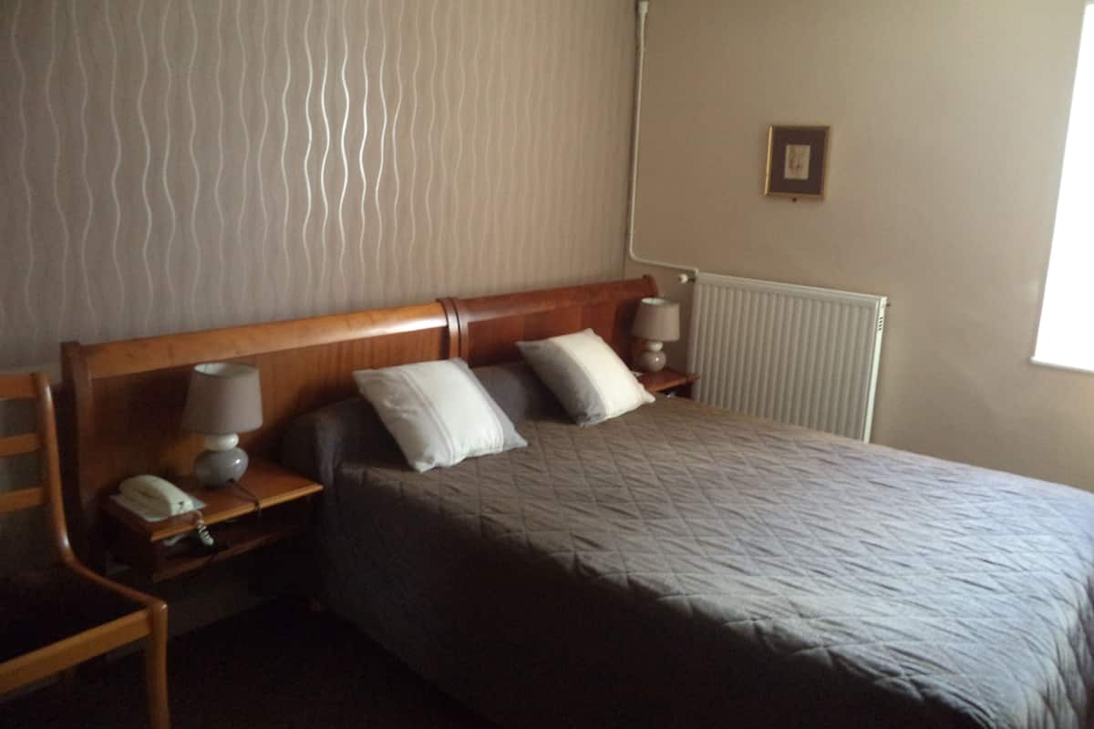 A neatly arranged hotel room with a bed, two bedside tables, a nightstand, a lamp, and a radiator.