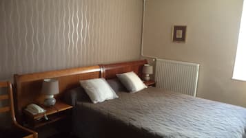 A neatly arranged hotel room with a bed, two bedside tables, a nightstand, a lamp, and a radiator.