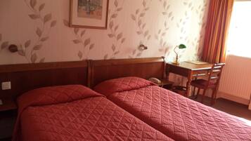 A hotel room with two beds, a desk, a chair, a lamp, and a window with curtains.