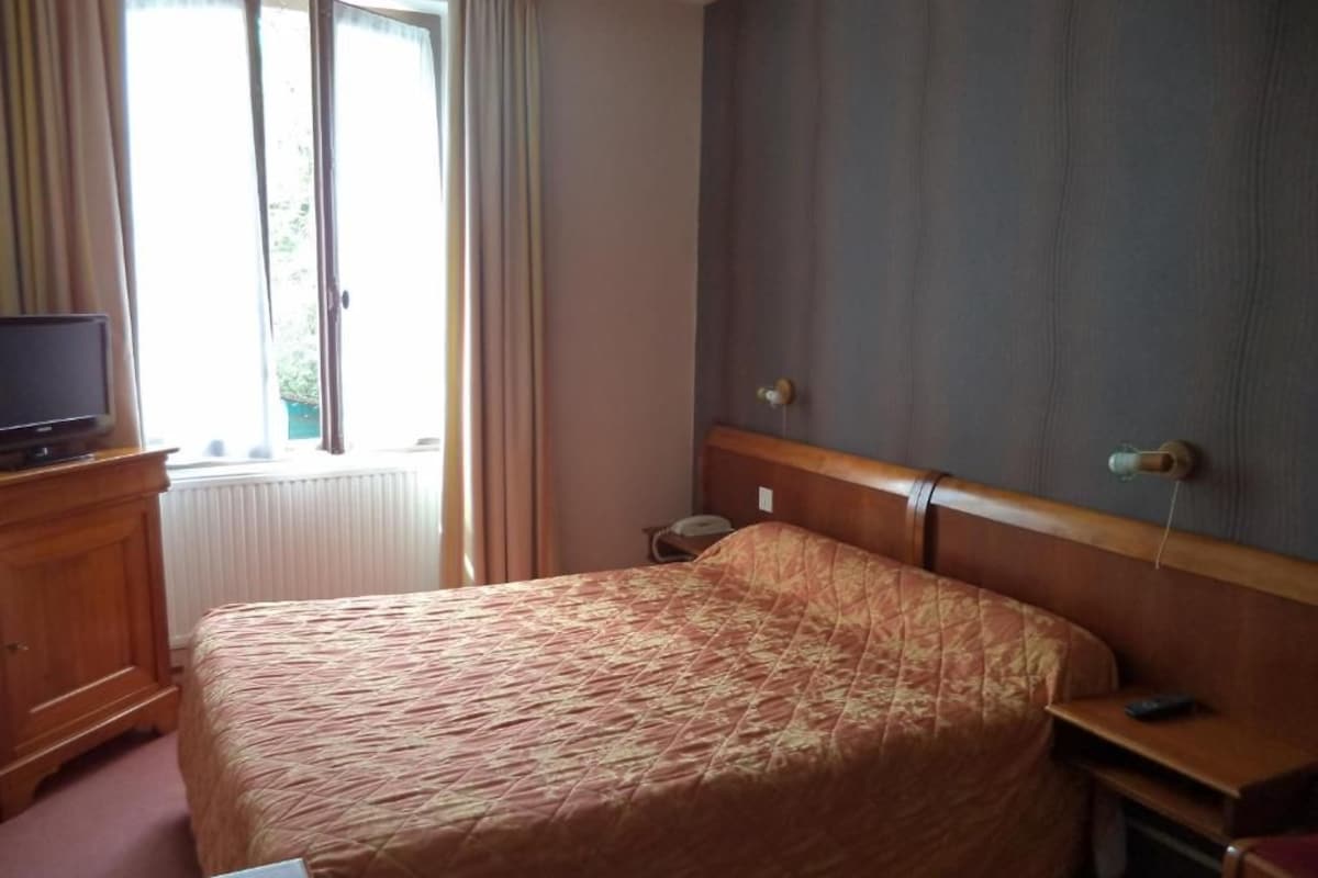 A hotel room with a bed, a wooden dresser, a television, and a window with curtains.