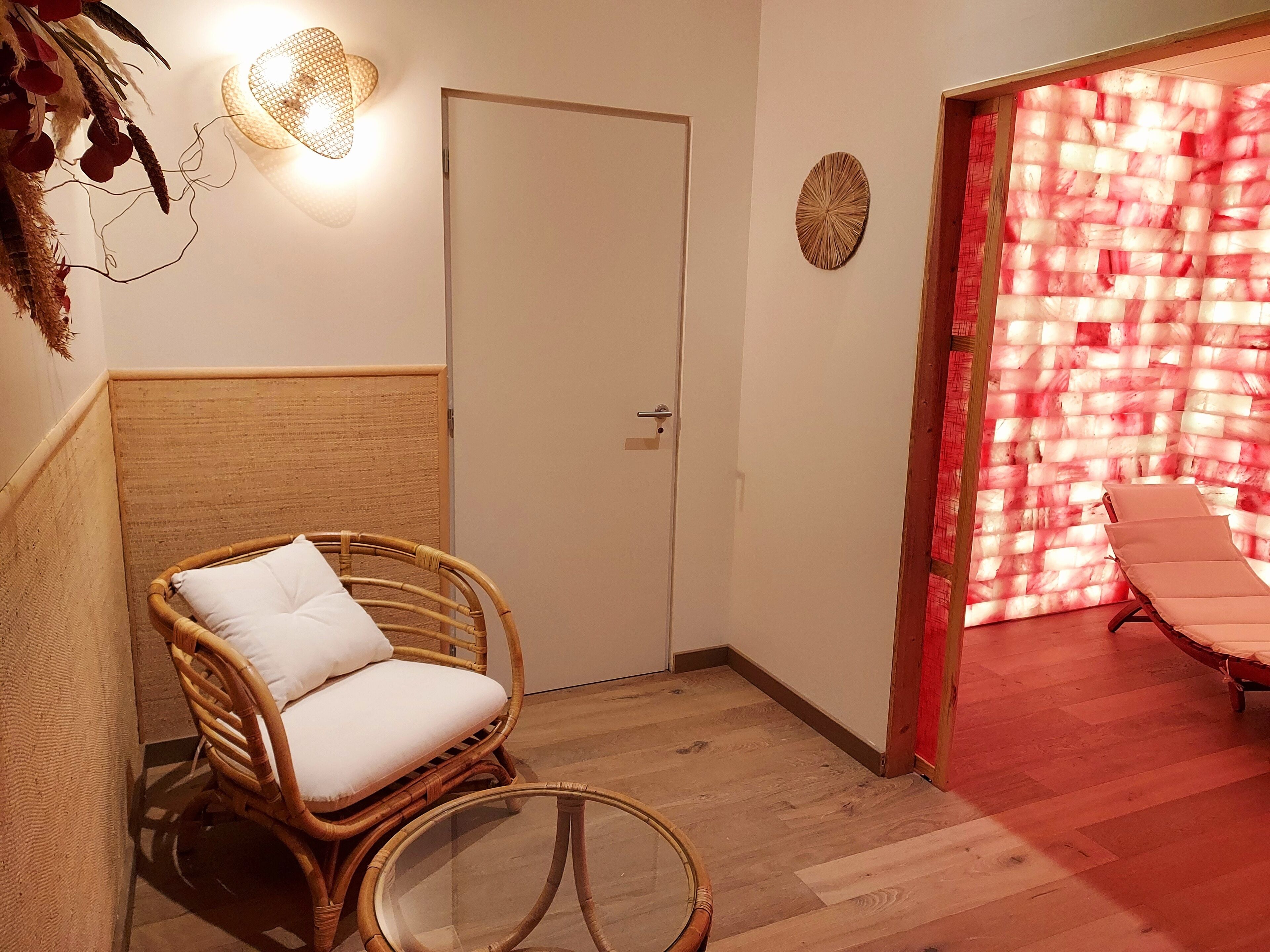 A room with a wicker chair, a glass table, a door, and a wall with a red and white pattern.