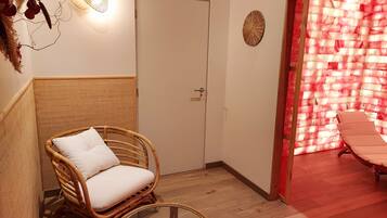 A room with a wicker chair, a glass table, a door, and a wall with a red and white pattern.