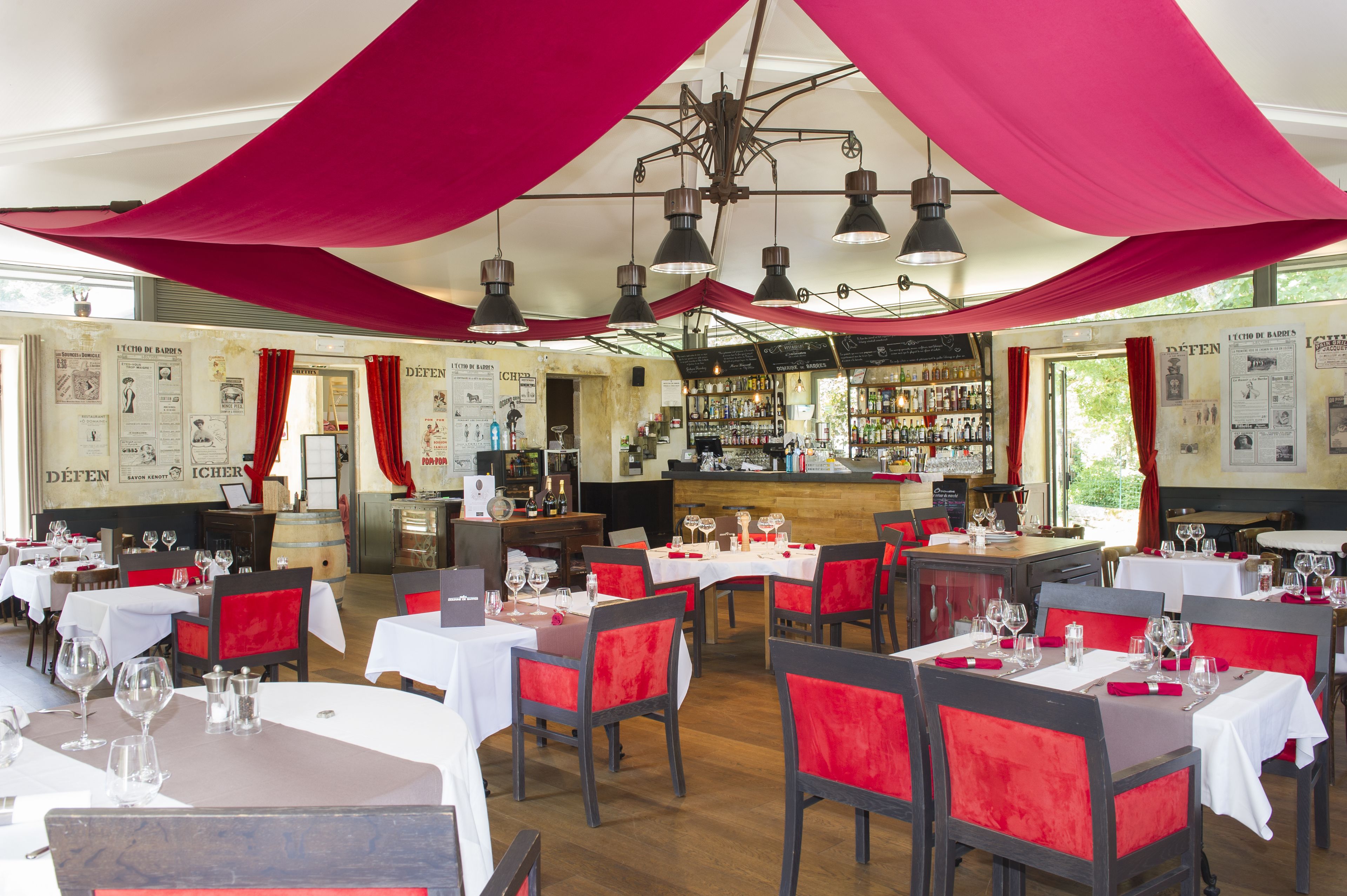 Un restaurante con mesas dispuestas para comer, una zona de bar y cortinas rojas colgadas del techo.