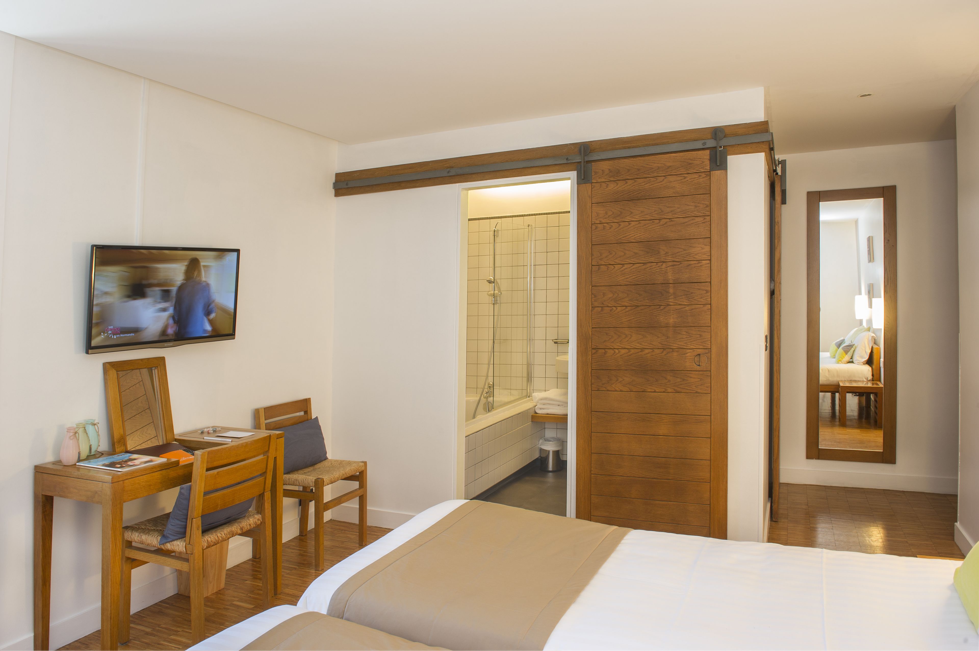 A bedroom with a bed, a desk with a chair, a television, and a bathroom with a shower and a mirror.