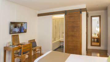 A bedroom with a bed, a desk with a chair, a television, and a bathroom with a shower and a mirror.