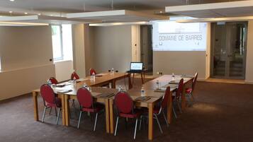Un salón de conferencias con una larga mesa, sillas rojas, una pantalla de proyector que muestra “DOMAINE DE BARRES” y un ordenador portátil sobre la mesa.