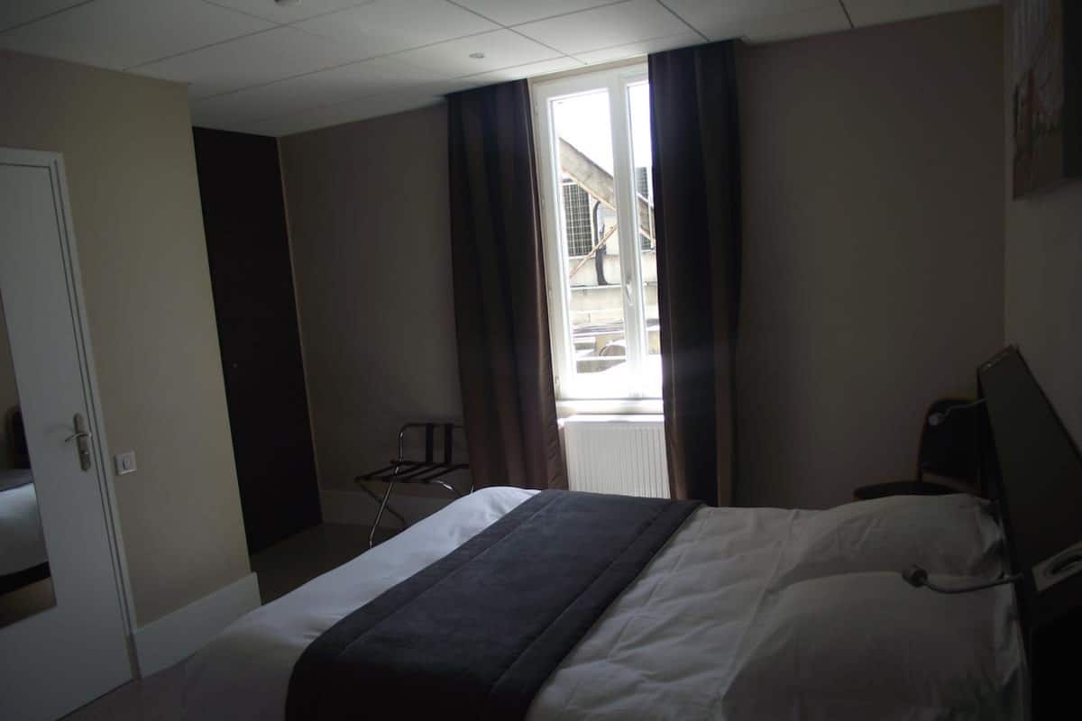 A hotel room with a bed, a desk, and a window with curtains.