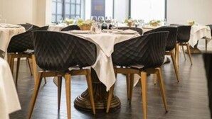 A dining area with round tables, black upholstered chairs, and a large crystal chandelier. - Hôtel des Bourbons (Montlucon)