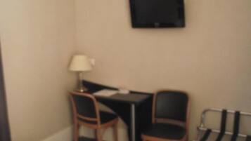 A hotel room with a bed, a desk with two chairs, a television mounted on the wall, and a luggage rack.